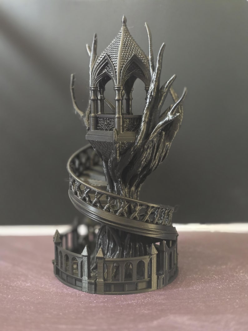Pode incluir: Uma escultura g&oacute;tica cinza escuro de um gazebo no topo de uma &aacute;rvore. O gazebo apresenta um telhado e uma varanda detalhados, com uma escada em espiral descendo pelo tronco. A base &eacute; cercada por uma cerca decorativa.