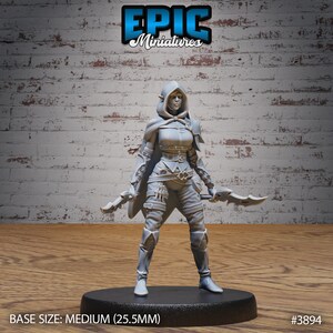 Puede incluir: Figurilla miniatura de pl&aacute;stico gris de una elfa femenina con una capa con capucha y sosteniendo dos dagas. La miniatura est&aacute; de pie sobre una base redonda con el texto "BASE SIZE: MEDIUM (25.5MM)" y "#3894" impreso en ella.