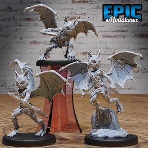 May include: Three gray painted miniature figurines of bat-like creatures with wings. The creatures are in various poses, one holding a dagger, one holding a staff, and one standing on a tombstone with the inscription "RIP".