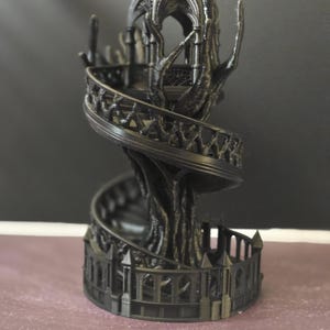 Pode incluir: Uma torre de fantasia preta impressa em 3D com uma escada em espiral e detalhes ornamentados. A torre apresenta uma estrutura semelhante a uma &aacute;rvore que suporta a escada e um topo semelhante a um gazebo. A base tem uma cerca decorativa.