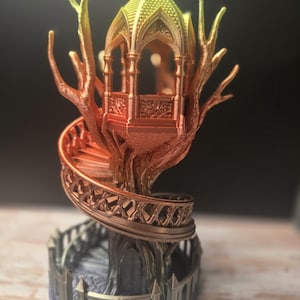 Pode incluir: Uma escultura de casa na &aacute;rvore de fantasia impressa em 3D com uma escada em espiral e uma estrutura semelhante a um gazebo no topo. A casa na &aacute;rvore apresenta um gradiente de cores, que vai do amarelo ao laranja e ao castanho. A base tem uma cerca cinzenta.