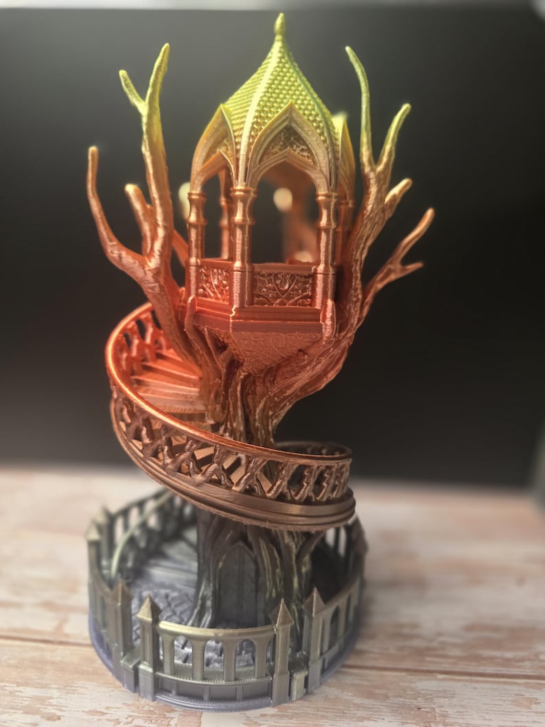Pode incluir: Uma escultura de casa na &aacute;rvore de fantasia impressa em 3D com uma escada em espiral e uma estrutura semelhante a um gazebo no topo. A casa na &aacute;rvore apresenta um gradiente de cores, que vai do amarelo ao laranja e ao castanho. A base tem uma cerca cinzenta.