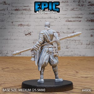 May include: A gray plastic miniature figurine of a person wearing a robe and holding a staff. The figurine is standing on a round base. The base is labeled "BASE SIZE: MEDIUM (25.5MM)" and "#4906".