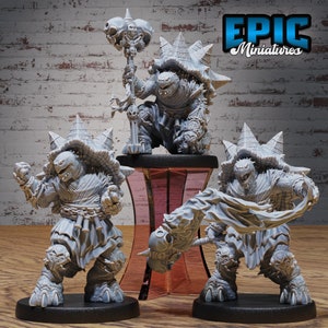 May include: Three grey, unpainted, miniature figurines of turtle-like creatures with spiky shells. The creature on the left is standing with its arms raised. The creature in the center is sitting with a staff in its hands. The creature on the right is standing with a banner in its hands. The miniatures are on black bases and are displayed on a pink pedestal. The text "EPIC Miniatures" is in the upper right corner of the image.