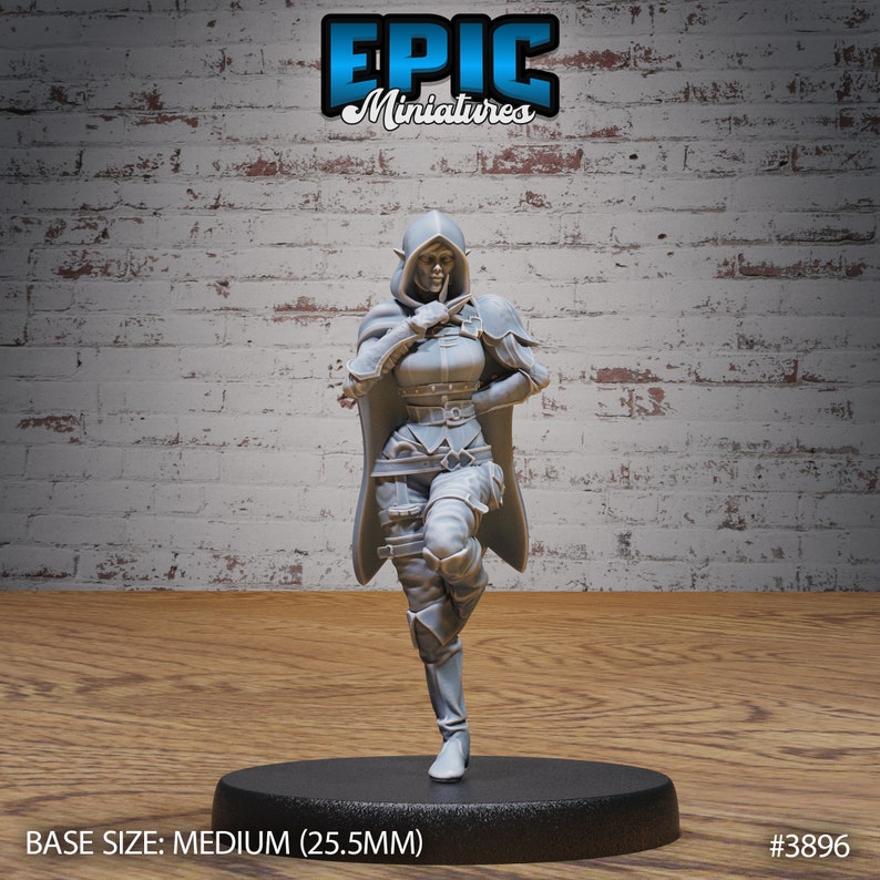 Puede incluir: Miniatura de elfo femenino impresa en 3D en gris, con una capa con capucha y sosteniendo una daga. La miniatura est&aacute; de pie sobre una base negra con el texto "BASE SIZE: MEDIUM (25.5MM)" y "#3896".