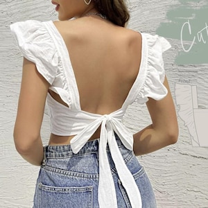 May include: A white crop top with a tie back and ruffled sleeves. The top is shown on a model wearing blue jeans. The image also includes a line drawing of the top's front and back, with the text "Cute Sleeve TOP" above the drawing.