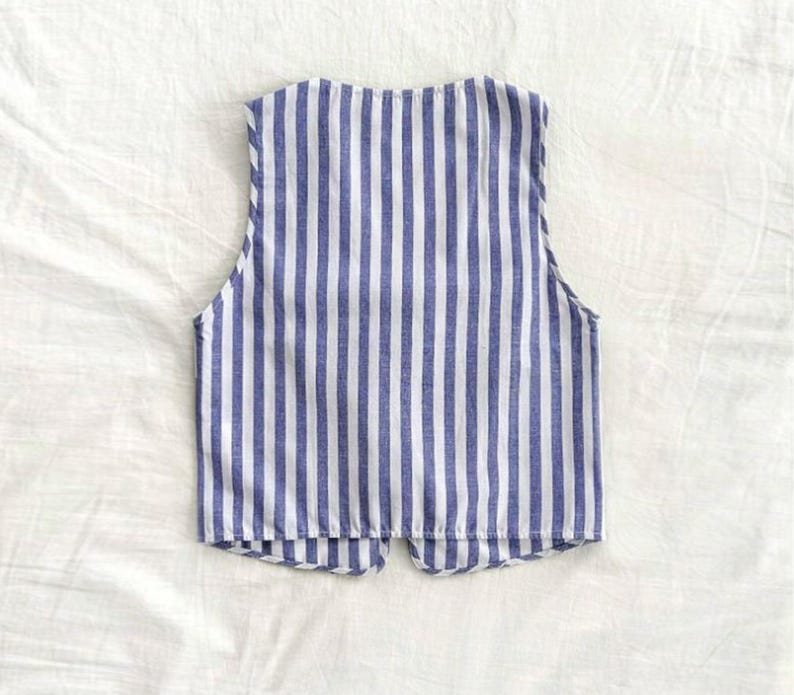 May include: A sleeveless vest with a blue and white striped pattern. The vest has a V-neck and a button closure.