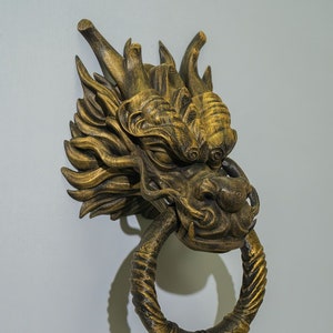 Könnte beinhalten: Ein goldener Türklopfer in Form eines Drachenkopfes mit einem detaillierten Design und einem Ringgriff.