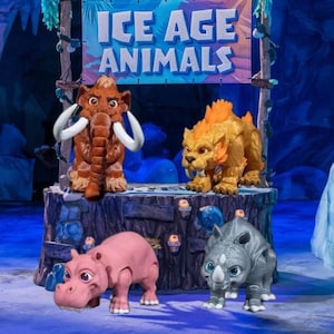 May include: A display featuring four Ice Age animal figurines: a brown mammoth with white tusks, a yellow saber-toothed tiger, a pink hippo, and a gray rhino. The sign above reads "ICE AGE ANIMALS".