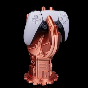 Può includere: Un controller PlayStation 5 bianco e nero è appoggiato su un supporto a forma di mano in stile steampunk, color rame. Il supporto presenta ingranaggi, rivetti e dettagli meccanici.
