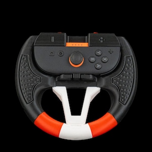 Może przedstawiać: Czarna i pomarańczowa kierownica do gier z białymi i czerwonymi akcentami. Kierownica posiada centralny panel sterowania z przyciskami i joystickiem. Projekt obejmuje teksturowany uchwyt na czarnym tle.