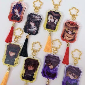 Puede incluir: Una colección de llaveros de personajes de estilo anime. Cada llavero presenta una ilustración de personaje diferente dentro de un marco rectangular. Los llaveros tienen cierres dorados en forma de estrella, borlas coloridas y la palabra "sample" está impresa en cada llavero.