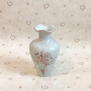 May include: A white ceramic vase with a pink floral design and a speckled glaze. The vase has a ruffled top and a rounded body.