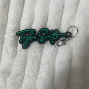 May include: Black keychain with a green "Taylor Swift" signature in a cursive font.