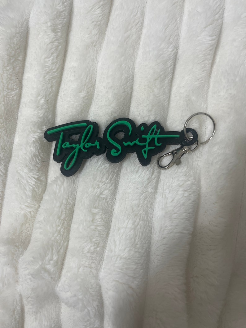May include: Black keychain with a green "Taylor Swift" signature in a cursive font.