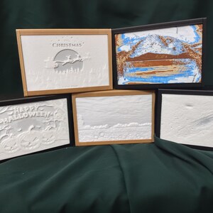 May include: Five framed 3D relief art pieces with different holiday themes. The frames are black and gold. The themes are Christmas, Halloween, a winter scene, a mountain scene, and a blank scene.