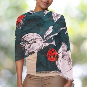 May include: A teal green scarf with a white floral pattern and red ladybugs. The scarf has a fringed edge.