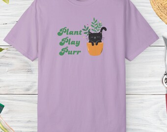 May include: A lavender t-shirt with a black cat sitting in a pot with green plants. The text "Plant Play Purr" is written in green on the shirt.