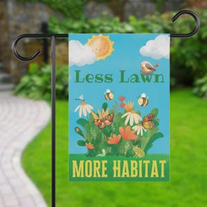 Puede incluir: Una bandera de jardín con fondo azul muestra el texto "Less Lawn More Habitat". La bandera presenta ilustraciones de un sol, nubes, flores, mariposas, abejas, un pájaro y una rana. La bandera está colgada de un soporte de metal negro.