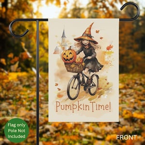 May include: A garden flag featuring a watercolor illustration of a girl in a witch hat riding a bicycle with pumpkins in a basket. The flag reads "Pumpkin Time!" in orange lettering. The background is a blurred autumn scene.