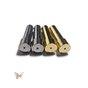 May include: Four cylindrical metal components arranged in a row. Two of the components have a silver-toned finish, while the other two have a gold-toned finish. Each component features a flat circular top with a small, centered hole.