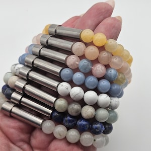 May include: A stack of bracelets with different colored gemstone beads and silver metal accents. The bracelets are arranged in a graduated pattern, with the largest bracelet at the bottom and the smallest bracelet at the top.