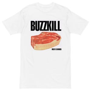 May include: White t-shirt with a graphic design. The design features the word "BUZZKILL" in bold black letters above a realistic illustration of a raw steak. Below the steak, the text reads "MEAT IS DINNER".