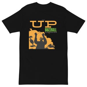May include: Black t-shirt with a graphic design featuring the word "UP" in orange, the word "BUZZKILL" in green, and a silhouette of a person with raised arms against an orange and yellow background.