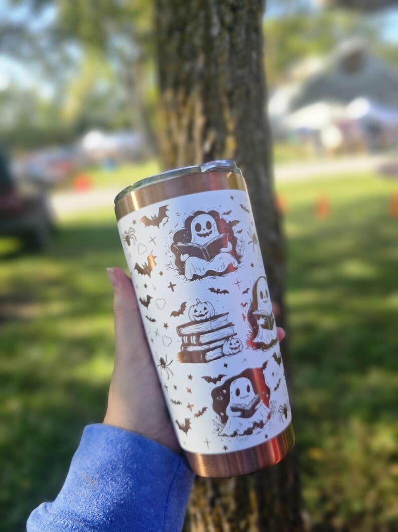 Puede incluir: Un vaso blanco y cobrizo con tem&aacute;tica de Halloween. El vaso est&aacute; decorado con ilustraciones de fantasmas, murci&eacute;lagos, ara&ntilde;as y calabazas. El dise&ntilde;o se repite alrededor del cuerpo del vaso.