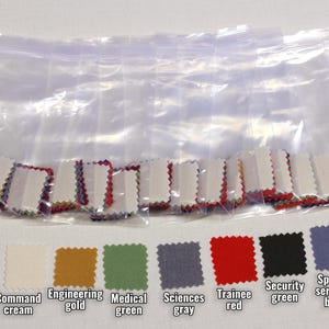 May include: A collection of fabric swatches in various colors, including maroon, cream, gold, green, gray, red, black, blue, and navy. The swatches are labeled with text such as "Monster maroon" and "ST5 commando blue". Some swatches are in a clear plastic bag.