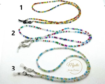 Puede incluir: Tres cadenas de gafas con cuentas en diferentes combinaciones de colores. La cadena superior es multicolor, la cadena del medio es azul, verde, rojo y blanco, y la cadena inferior es blanca, azul y verde. Cada cadena tiene cierres para sujetar a las gafas.