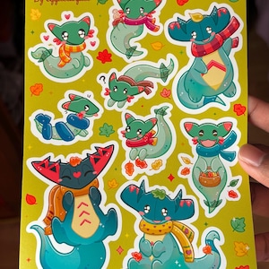 Könnte beinhalten: Ein Stickerbogen mit Cartoon-Kreaturen mit türkisfarbenen Körpern und grünen Köpfen, die Schals tragen und von Herbstblättern umgeben sind. Die Kreaturen sind in verschiedenen Posen auf einem gelb-grünen Hintergrund. Der Text "By Applelunpiee" steht oben.