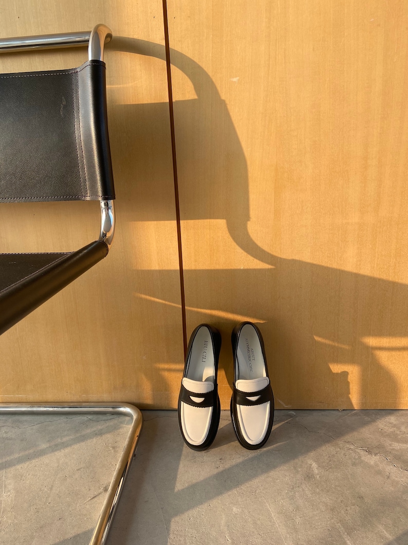 May include: A pair of black and white leather loafers with a white leather trim and the word "HILLCITY" printed on the side.