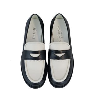 May include: A pair of black and white leather loafers with a contrasting color design. The loafers have a black leather upper with a white leather toe and heel. The text "BIU CILI" is printed on the inside of the left shoe and "ASYMMETRIC" is printed on the inside of the right shoe.