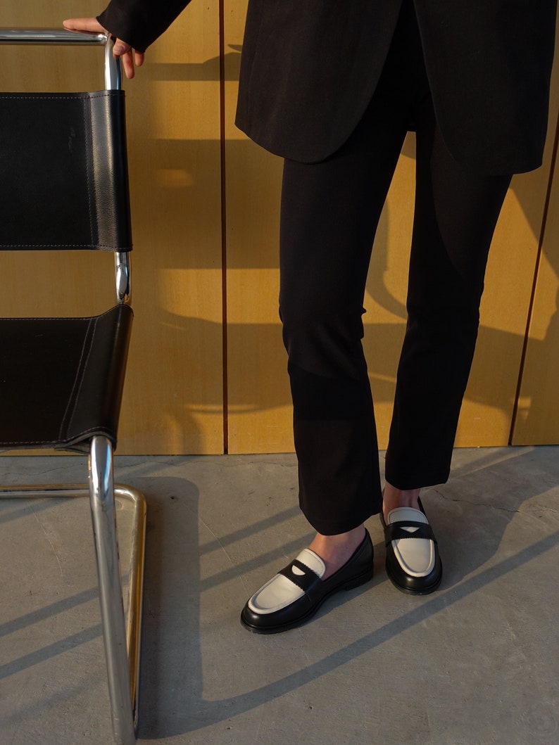 May include: A person wearing black pants and a black blazer with white loafers. The loafers have a black and white color block design.