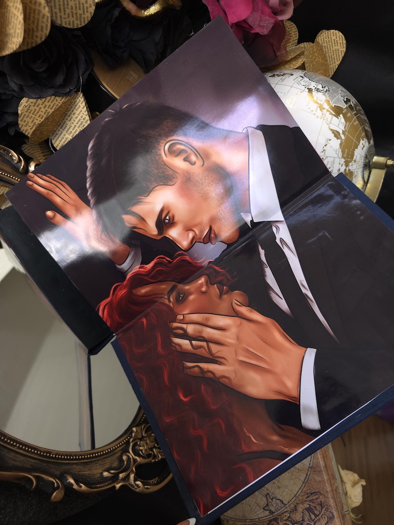 May include: Two books with illustrations of a man in a black suit and a woman with red hair. The man is leaning over the woman, with his hand covering her mouth. The books are on a dark surface with decorative elements.