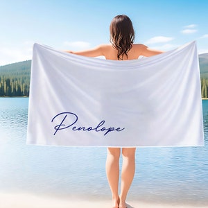 May include: White beach towel with the name "Penelope" written in blue cursive script.
