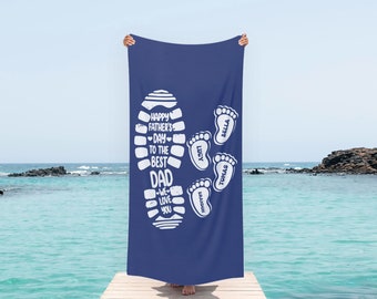 May include: A blue beach towel with a white footprint design. The footprint has the text "Happy Father's Day to the Best Dad" and four smaller footprints with the names "Bella", "Lucy", "Thomas", and "Braxton".