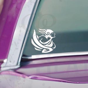 Puede incluir: Calcoman&iacute;a de vinilo blanco de una figura cl&aacute;sica con cabello suelto y ropa drapeada. La calcoman&iacute;a est&aacute; adherida a la ventana de un autom&oacute;vil, con la pintura p&uacute;rpura del veh&iacute;culo visible. El dise&ntilde;o es una silueta.