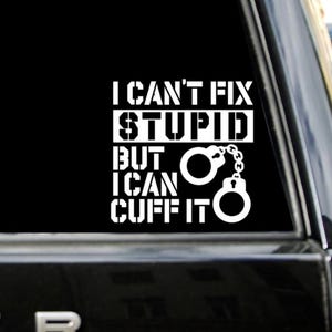 May include: White vinyl decal with the text "I CAN'T FIX STUPID BUT I CAN CUFF IT" and a handcuff graphic. The decal is displayed on a black background, likely a car window.