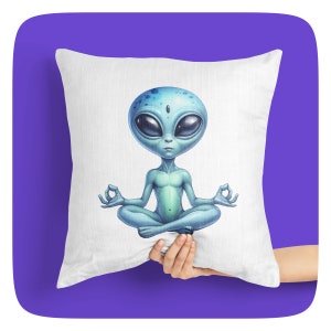 Puede incluir: Una almohada blanca con un extraterrestre azul meditando en una postura de yoga. El extraterrestre tiene ojos grandes y un tercer ojo en la frente.