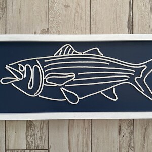 May include: A rectangular wall art piece with a white frame, navy blue background, and a white rope fish design. This nautical-themed artwork is suitable for coastal decor and measures approximately 60cm in length.