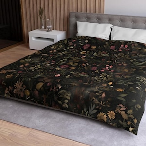 May include: A black duvet cover with a floral pattern featuring pink, yellow, and green flowers and leaves. The duvet cover is on a bed with white pillows and a gray headboard.