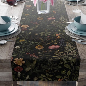 May include: A black table runner with a floral pattern featuring pink, yellow, and red flowers. The runner is on a wooden table with two place settings on each side.