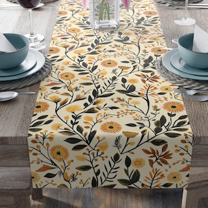 Könnte beinhalten: Ein gelber Blumen-Tischläufer mit einem sich wiederholenden Muster aus dunkelgrünen Blättern und orangefarbenen Blüten. Der Läufer liegt auf einem Holztisch mit Gedecken auf beiden Seiten.