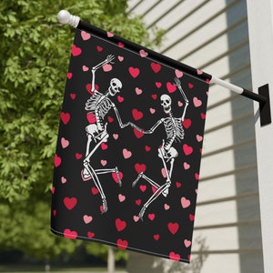 Könnte beinhalten: Eine schwarze Flagge mit zwei weißen Skeletten, die mit rosafarbenen Herzen auf schwarzem Hintergrund tanzen.