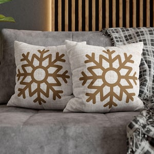 May include: Two white throw pillows with brown snowflake designs on a gray couch with a black and white plaid throw blanket.