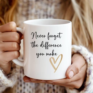May include: White ceramic coffee mug with a black inscription that reads "Never forget the difference you make" and a gold heart design.