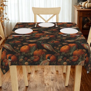 Puede incluir: Un mantel rectangular con un estampado de temática otoñal. El diseño presenta calabazas, faisanes y follaje en tonos naranja, marrón y verde. Platos y cubiertos blancos están colocados sobre la mesa, que está sostenida por patas de madera clara.