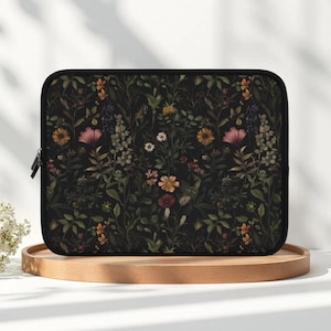 May include: Black laptop sleeve featuring a floral pattern with pink, yellow, and orange flowers, along with green leaves. The sleeve has a black zipper and a black border. The design is set against a dark background.